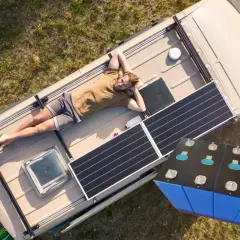 Mężczyzna odpoczywa na dachu kampera z panelami słonecznymi, obok magazyn energii 15 kWh.