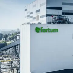 Nowoczesna elektrociepłownia Fortum, gdzie powstaje zielony prąd, z charakterystycznym logo. W tle widać kominy i chłodnie kominowe.