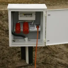 Skrzynka elektryczna na działce bez domu, gotowa do podłączenia prądu. Widoczne gniazda i zabezpieczenia.