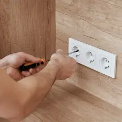 Ręce przykręcają gniazdko elektryczne. Dbałość o prawidłowe podłączenie zapewni bezpieczny **napięcie skuteczne**.