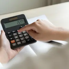 Dłoń naciska przycisk kalkulatora z widocznym wynikiem 264.75.