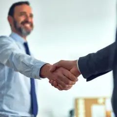 Uśmiechnięty mężczyzna w koszuli i krawacie ściska dłoń partnerowi biznesowemu. Pozytywne axpo polska opinie potwierdzone gestem.
