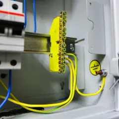 Wnętrze rozdzielnicy elektrycznej z widocznym żółtym listwą zaciskową i przewodami, symbolizującymi pomiar rezystancji uziemienia.