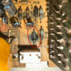 Uszkodzony rezystor z czerwonym okręgiem, otoczony innymi elementami elektronicznymi na płytce drukowanej.
