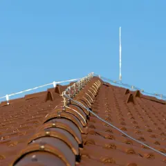 Na brązowym dachu widoczna jest instalacja odgromowa z przewodami i piorunochronami, chroniąca budynek przed uderzeniami pioruna.