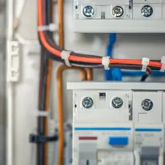 Wnętrze rozdzielnicy elektrycznej z przewodami w kolorach pomarańczowym i brązowym, zabezpieczonymi opaskami. Widoczne wyłączniki i zaciski.