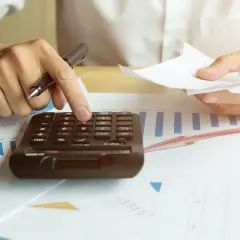 Rachunki za prąd rosną. Dłoń z długopisem liczy na kalkulatorze, analizując wykresy.