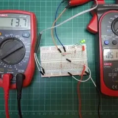 Układ na płytce stykowej z diodą Zenera, dwoma multimetrami i diodami LED. Jeden multimetr pokazuje 13.7V, drugi 0.516A.