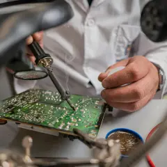 Ręce technika lutują płytę główną pod lupą. Nawet w **zimne luty** praca wre, by naprawić elektronikę.