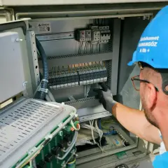 Elektryk w niebieskim kasku pracuje przy skrzynce elektrycznej. To oświadczenie o gotowości instalacji przyłączanej.