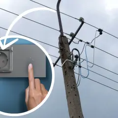 Ręka naciska przycisk obok gniazdka, sugerując koszt instalacji elektrycznej. W tle słup energetyczny z przewodami.