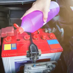 Ręka wlewa elektrolit do akumulatora samochodowego.