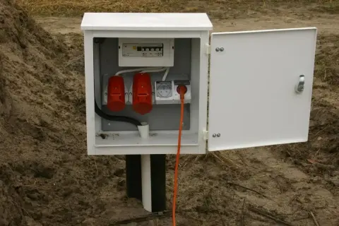 Skrzynka elektryczna na działce bez domu, gotowa do podłączenia prądu. Widoczne gniazda i zabezpieczenia.
