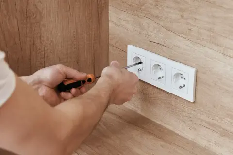 Ręce przykręcają gniazdko elektryczne. Dbałość o prawidłowe podłączenie zapewni bezpieczny **napięcie skuteczne**.