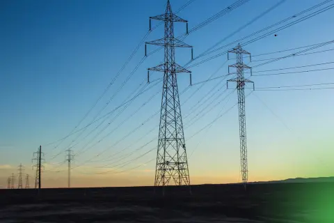 Wieże energetyczne niosące prąd przemienny na tle zachodzącego słońca.