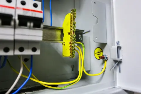 Wnętrze rozdzielnicy elektrycznej z widocznym żółtym listwą zaciskową i przewodami, symbolizującymi pomiar rezystancji uziemienia.