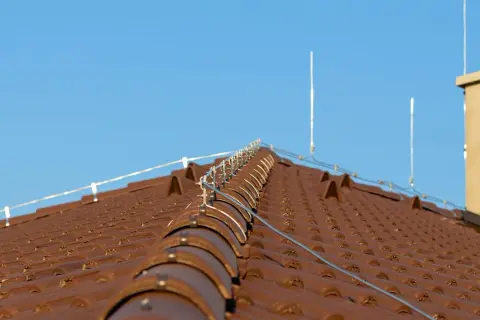 Na brązowym dachu widoczna jest instalacja odgromowa z przewodami i piorunochronami, chroniąca budynek przed uderzeniami pioruna.