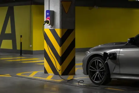 Szary samochód elektryczny ładuje się przy wallboxie. Ranking firm montujących ładowarki do samochodów elektrycznych.