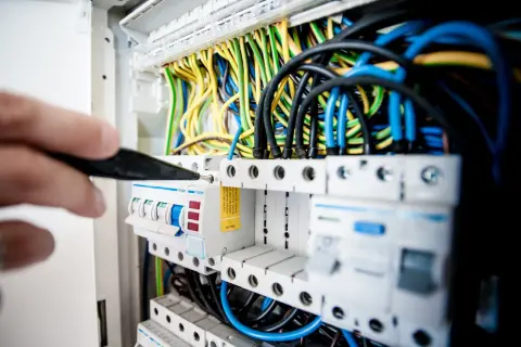 Ręka z narzędziem przy skrzynce z bezpiecznikami. Sprawdzanie instalacji elektrycznej to pierwszy krok, jak sprawdzić gdzie jest awaria prądu.