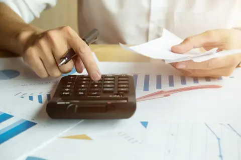 Rachunki za prąd rosną. Dłoń z długopisem liczy na kalkulatorze, analizując wykresy.