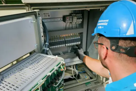 Elektryk w niebieskim kasku pracuje przy skrzynce elektrycznej. To oświadczenie o gotowości instalacji przyłączanej.