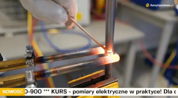 Ręka w rękawiczce wykonuje lutowanie miedzi. Dwa rozgrzane do czerwoności miedziane przewody są łączone za pomocą cienkiego drutu.