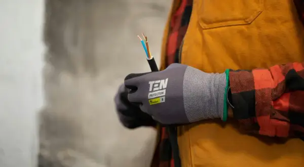 Elektryk w rękawicach trzyma kabel z odsłoniętymi przewodami.