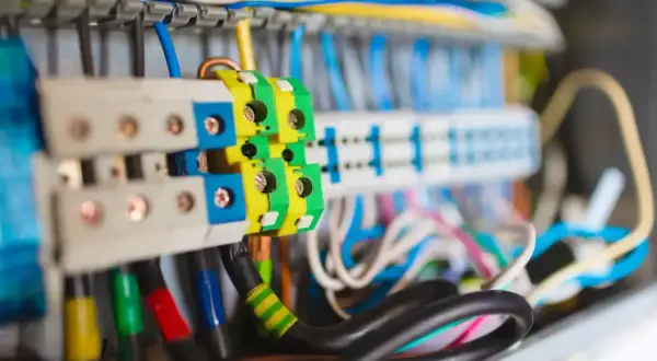 Kolorowe przewody w skrzynce elektrycznej, w tym zielono-żółty przewód uziemienia, łączą się z zaciskami.