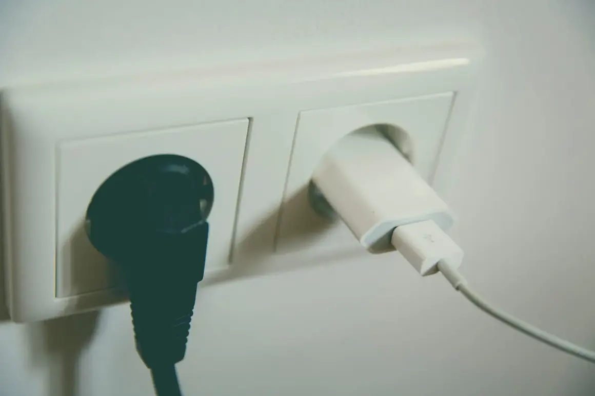 Dwa gniazdka elektryczne. W jednym czarna wtyczka, w drugim biała ładowarka z kablem. Napięcie w gniazdku zasila urządzenia.
