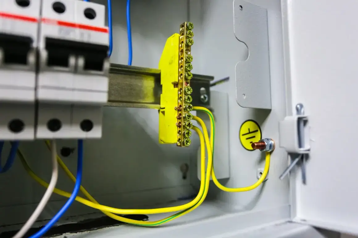 Wnętrze rozdzielnicy elektrycznej z widocznym żółtym listwą zaciskową i przewodami, symbolizującymi pomiar rezystancji uziemienia.