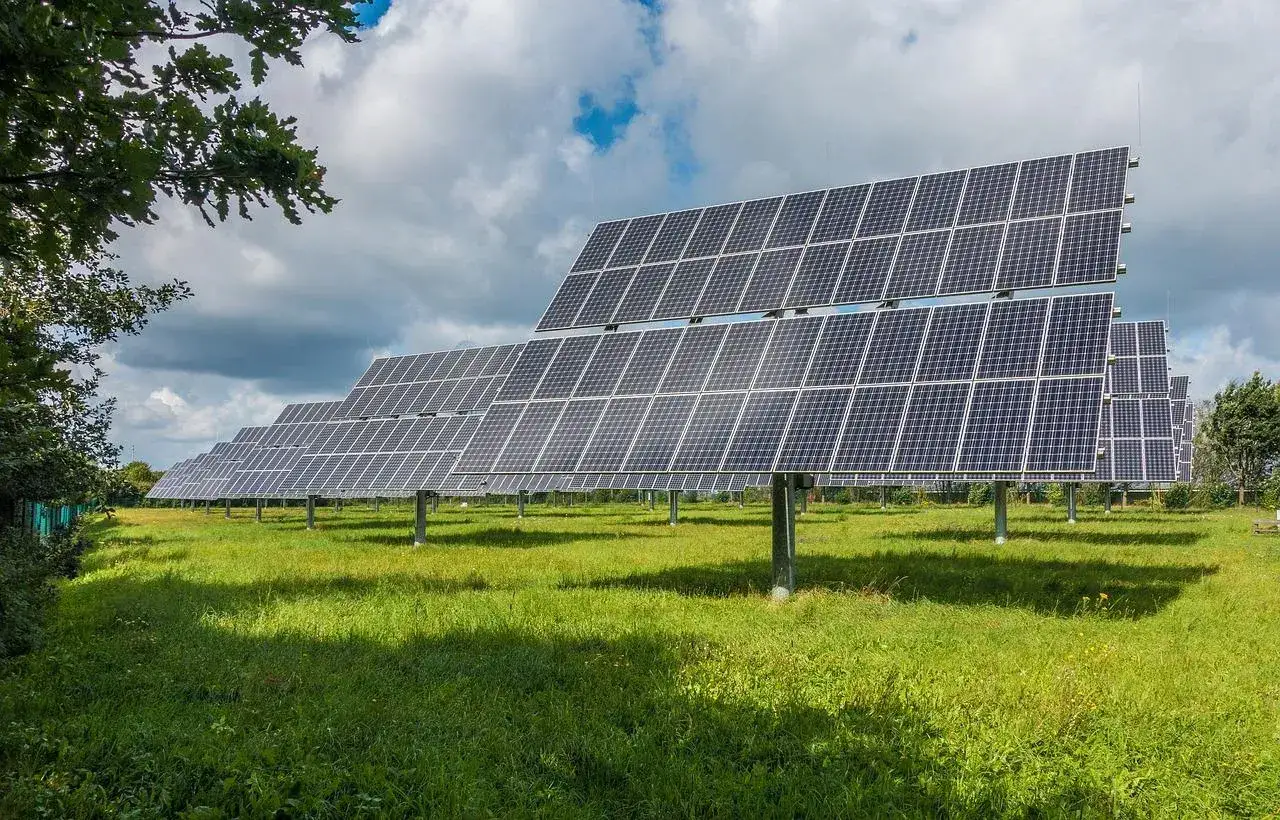Rzędy paneli fotowoltaicznych na zielonej łące, łapiące słońce. Ta farma fotowoltaiczna to przyszłość energii.