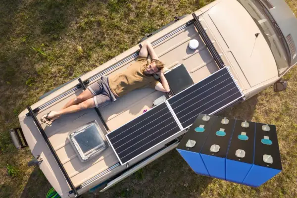 Mężczyzna odpoczywa na dachu kampera z panelami słonecznymi, obok magazyn energii 15 kWh.