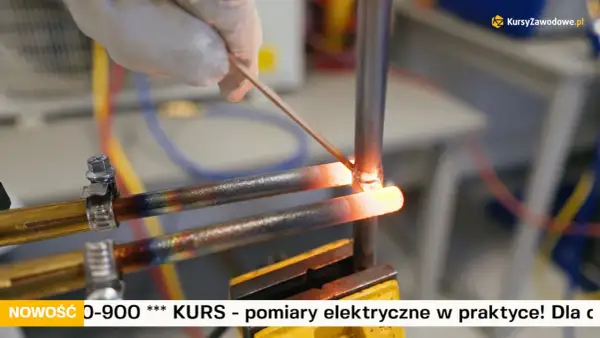 Ręka w rękawiczce wykonuje lutowanie miedzi. Dwa rozgrzane do czerwoności miedziane przewody są łączone za pomocą cienkiego drutu.
