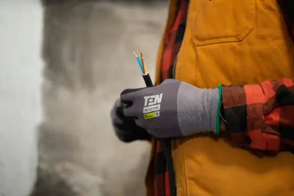 Elektryk w rękawicach trzyma kabel z odsłoniętymi przewodami.