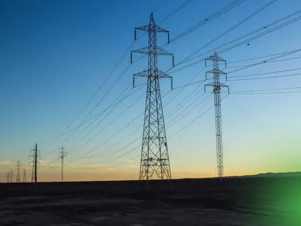 Wieże energetyczne niosące prąd przemienny na tle zachodzącego słońca.