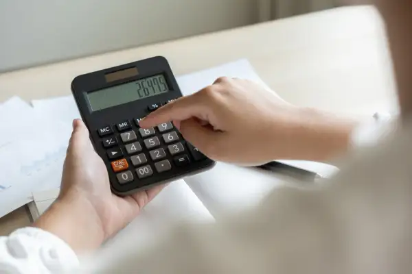 Dłoń naciska przycisk kalkulatora z widocznym wynikiem 264.75.