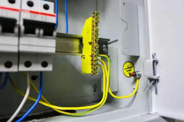 Wnętrze rozdzielnicy elektrycznej z widocznym żółtym listwą zaciskową i przewodami, symbolizującymi pomiar rezystancji uziemienia.