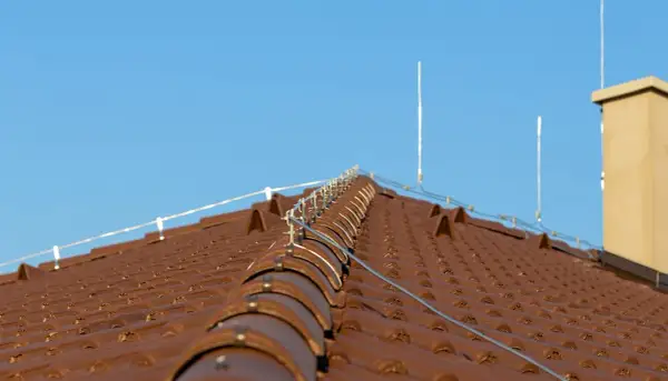 Na brązowym dachu widoczna jest instalacja odgromowa z przewodami i piorunochronami, chroniąca budynek przed uderzeniami pioruna.