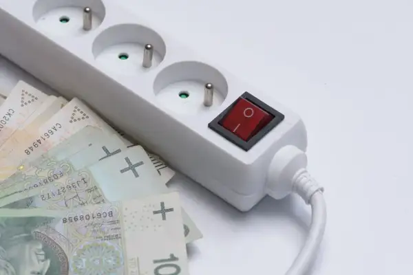 Biała listwa zasilająca z czerwonym włącznikiem i polskimi banknotami. Taki dodatek do prądu może oznaczać wysokie rachunki.