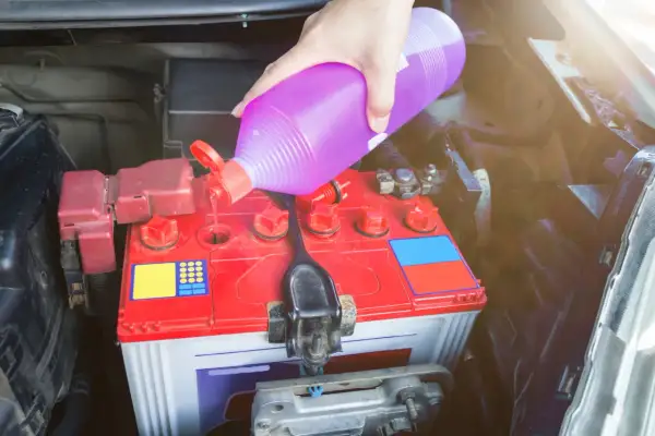 Ręka wlewa elektrolit do akumulatora samochodowego.
